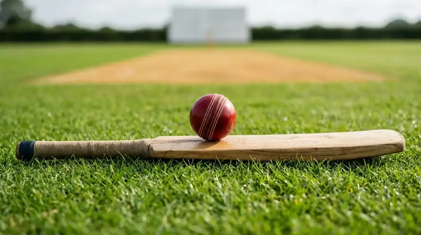 A cricket bat and red ball resting on freshly cut grass at an English ground